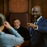 attorney suit standing and gesturing while addressing woman in courtroom with judge seated in background during legal proceedings cross examination tips for witnesses