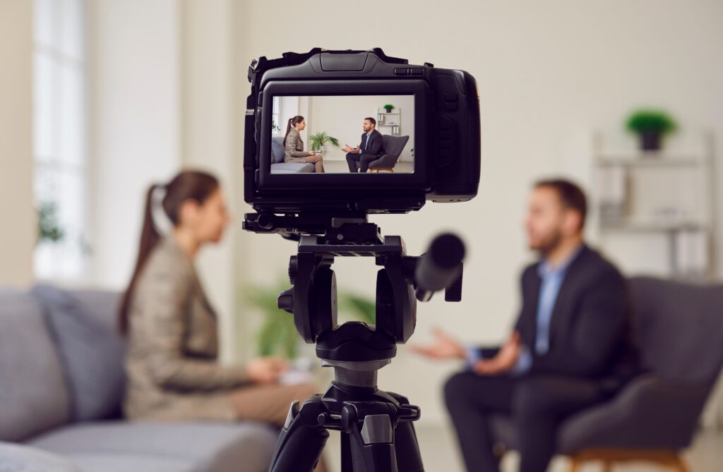 Camera,On,Tripod,Foreground,,Businessman,Giving,Interview,To,Journalist,In