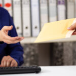 person sitting in front of a computer and keyboard being handed an envelope for service of process