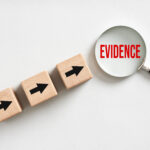 Wooden cubes with black arrows pointing at the word evidence under magnifying glass on white background